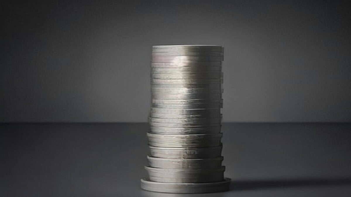 Pila de monedas plateadas sobre una superficie gris.