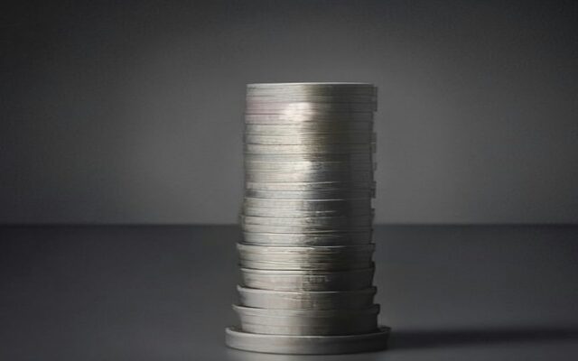 Pila de monedas plateadas sobre una superficie gris.