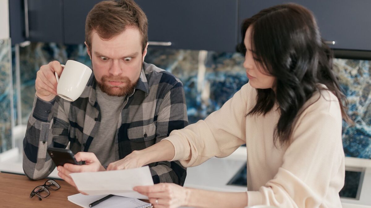 Una pareja revisa cuentas del hogar en la cocina con calculadora y documentos