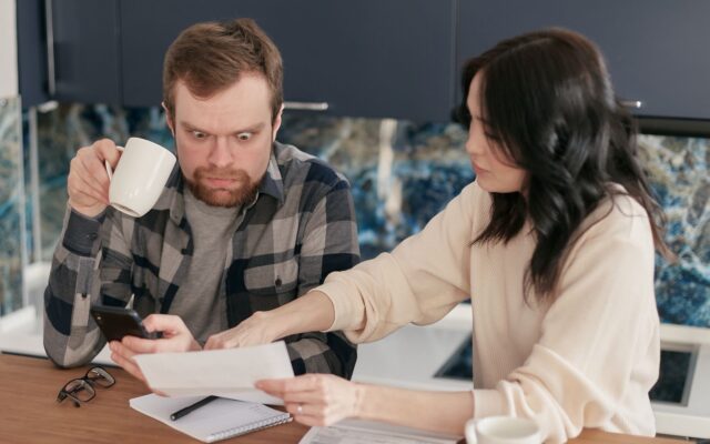 Una pareja revisa cuentas del hogar en la cocina con calculadora y documentos