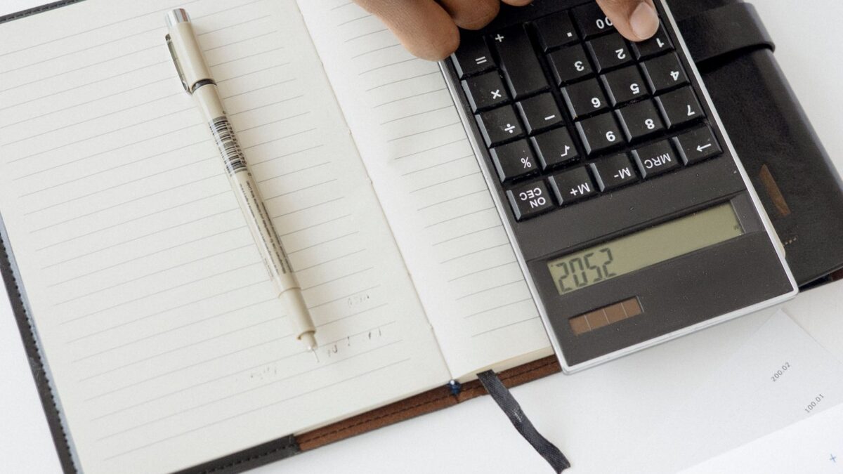 Una mano usa una calculadora junto a documentos financieros y un cuaderno