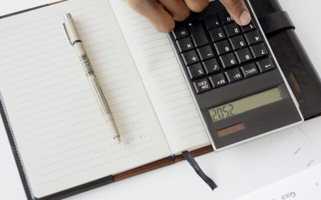 Una mano usa una calculadora junto a documentos financieros y un cuaderno