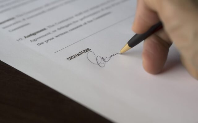 Una mano firma un contrato sobre un escritorio de madera