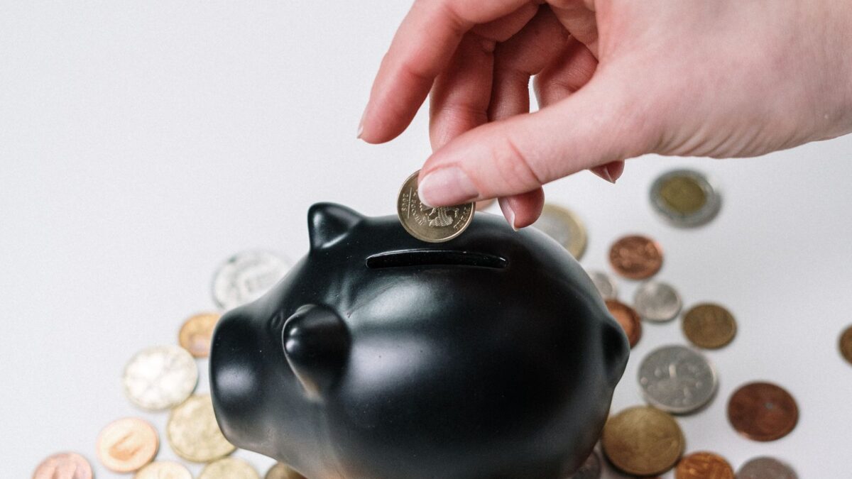 Una mano deposita una moneda en una alcancía rodeada de monedas