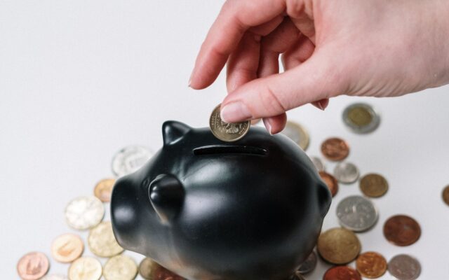 Una mano deposita una moneda en una alcancía rodeada de monedas